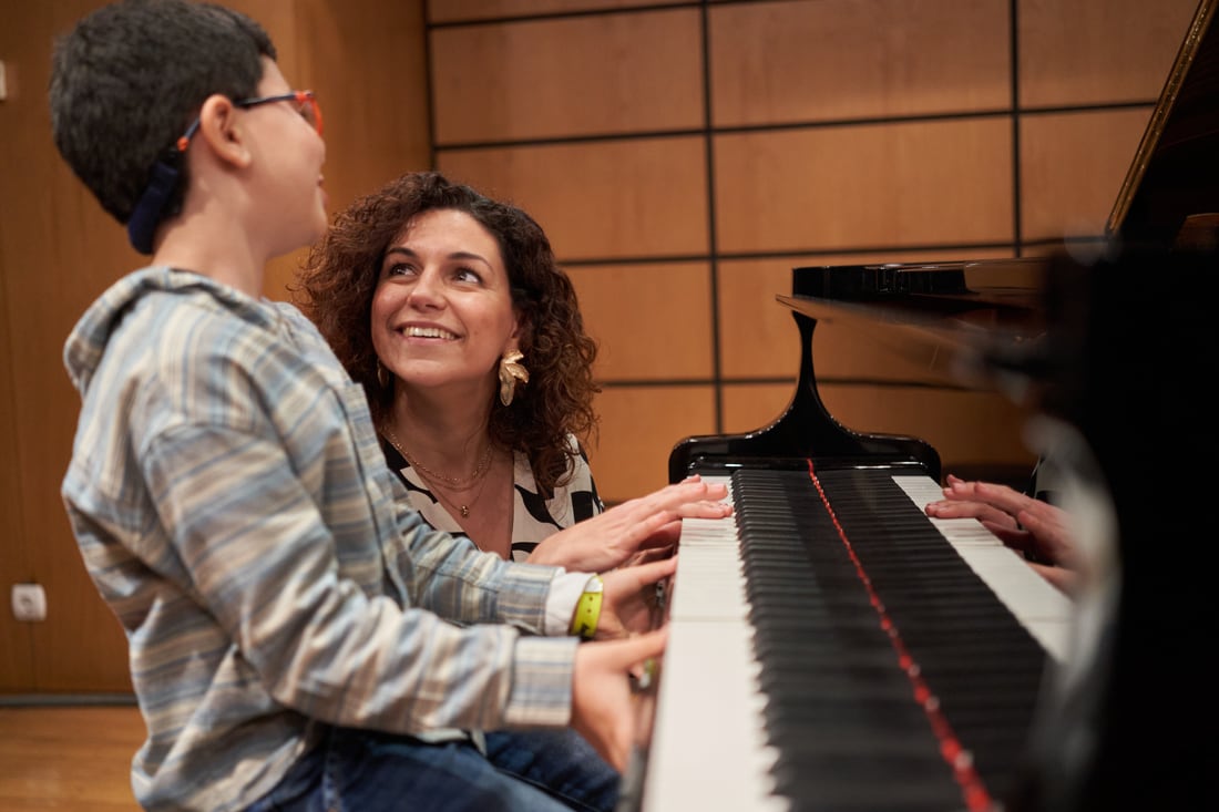 Gabriela Fernandes com jovem aluno ao piano